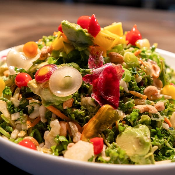 Close-up of a vibrant Thai salad with mixed greens, cherry tomatoes, avocado, cashews, and peppers.