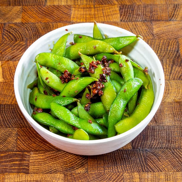 A white bowl filled with vibrant green edamame pods, topped with a savory brown seasoning.