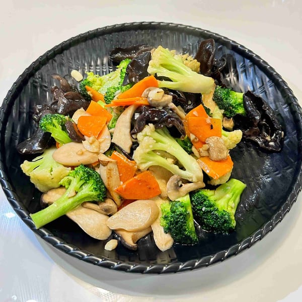 Stir-fried mixed vegetables with broccoli, carrots, mushrooms, and wood ear mushrooms on a black plate.