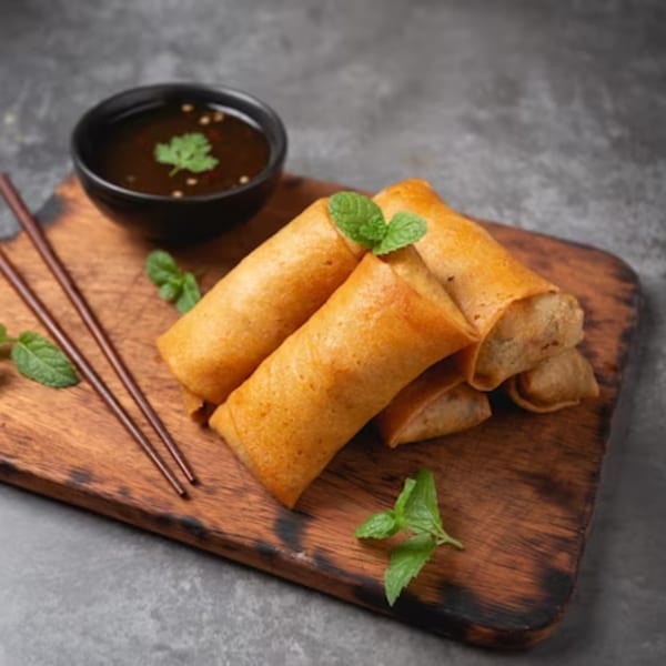 Crispy Thai spring rolls with mint garnish, chopsticks, and dipping sauce on a wooden board.