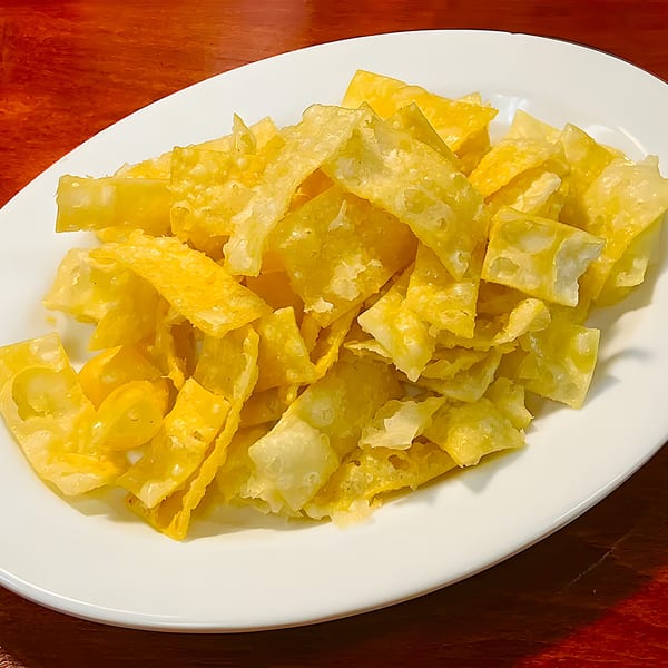 A white oval plate filled with golden-brown, crispy Thai fried wonton strips on a wooden table.